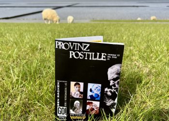 Im Vordergrund sit die Provinzpostille mit einem schwarzen Titelbild mit Schriftzug Provinz Postille und Fotos von einer perosn mit einem papaufsteller zu sehen. Im Hintergrund grasen Schafe und das Watt bei Ebbe ist sichtbar.