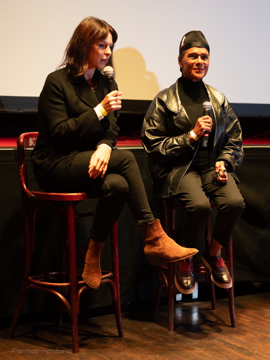 Pauline Black und die Regisseurin sitzen auf Barhockern vor der Leinwand u8nd haben Mikrofone in der Hand