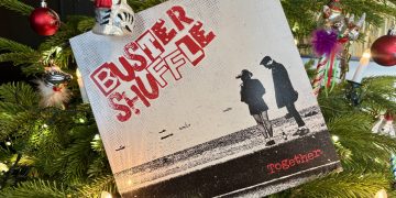 Das Cover in schwarz weiß mit roter Schrift "Buster Shuffle - Together", zeigt die Silhouette von zwei Menschen, die auf ein Gewässer mit Schiffen schauen. Im Hintergrund ist ein beleuchteter Tannenbaum zu sehen mit Weihnachtsschmuck.