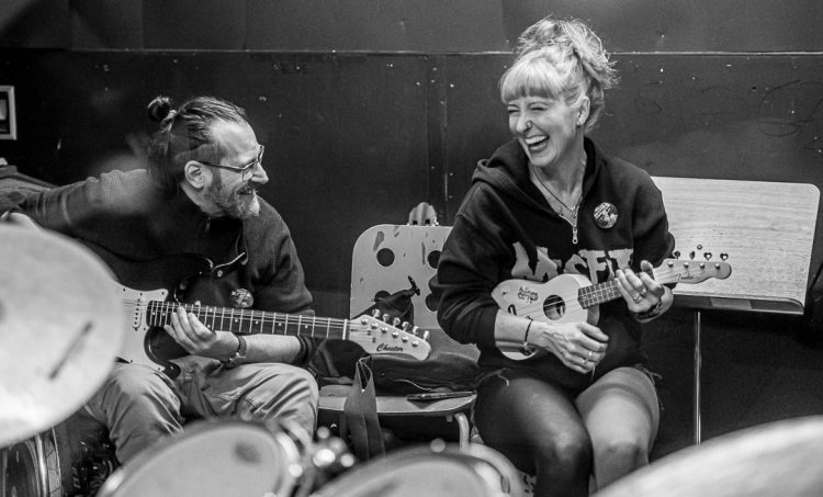 MusInclusion #34 - Band Workshop und so viele weitere coole Dinge! 1 Zwei Personen mit Musikinstrumenten, eine Ukulele und eine Gitarre; sitzen zusammen und lachen.