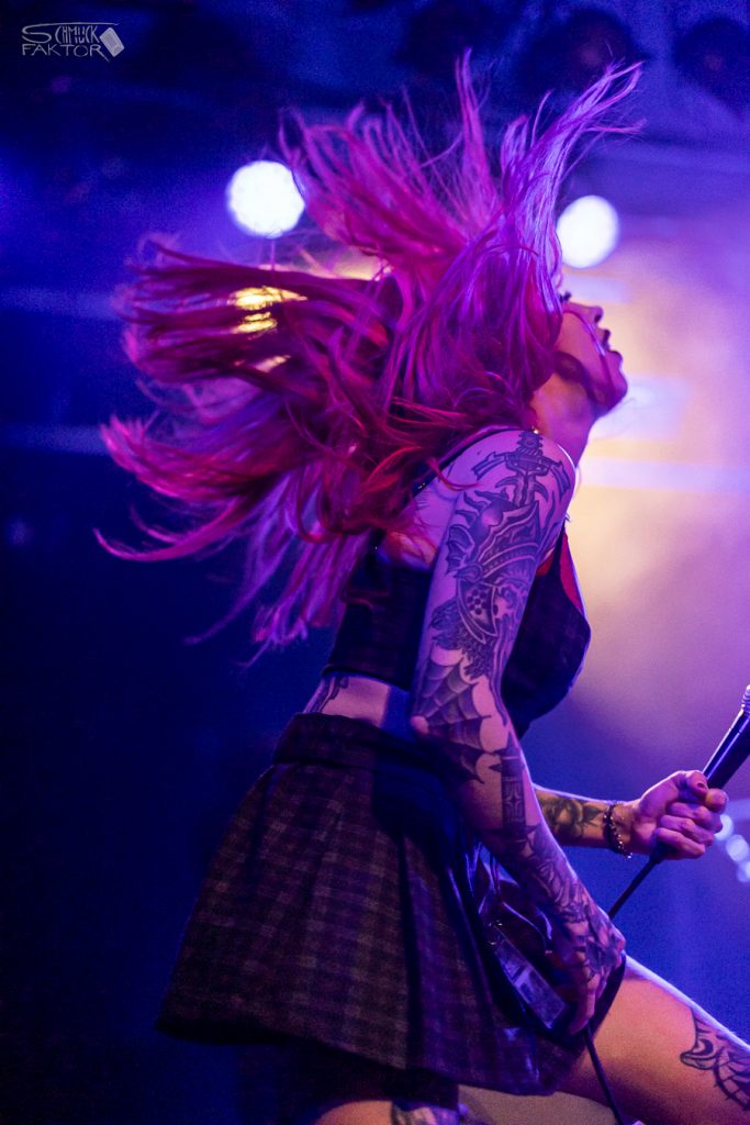 Interview mit Gero / Female Fronted is not a Genre Festival 2026 19 Eine Person mit langen roten Haaren schleudert diese in blau-violettem Licht mit gelber Gegenlichtquelle in die Luft