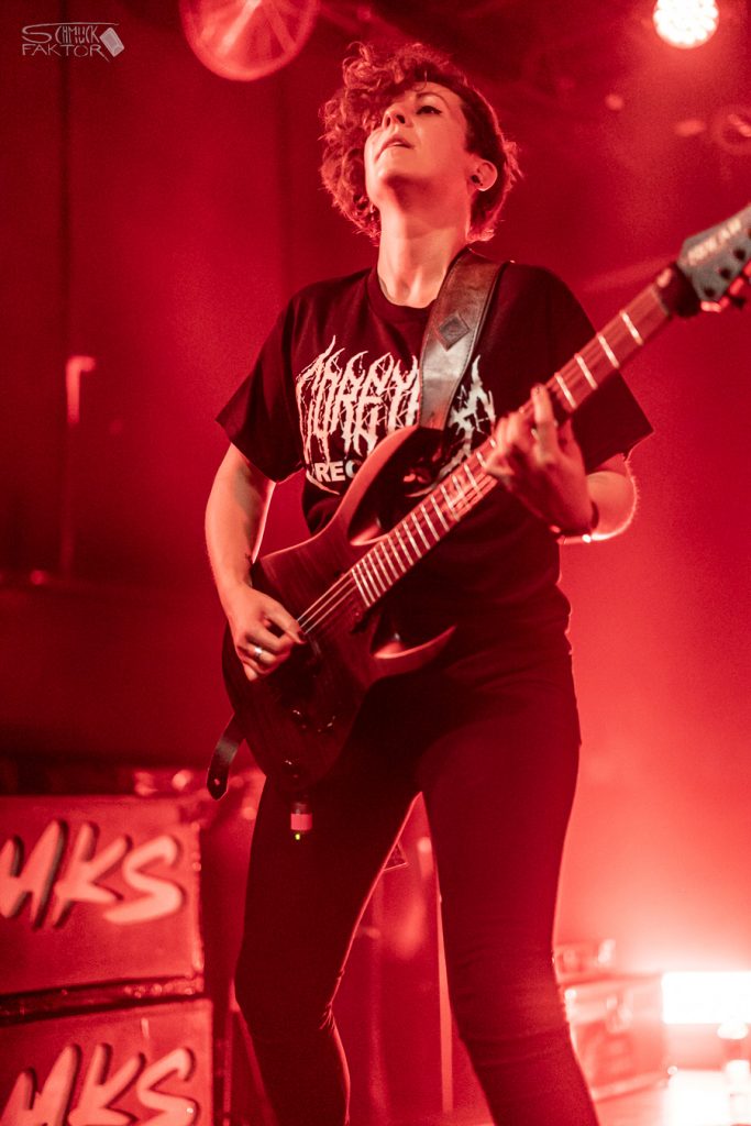 Interview mit Gero / Female Fronted is not a Genre Festival 2026 11 Eine Gitarristin spielt mit zurückgeworfenem Kopf und wilder Lockenmähne auf ihrer Gitarre. Sie trägt ein schwarz-weißes Bandshirt.