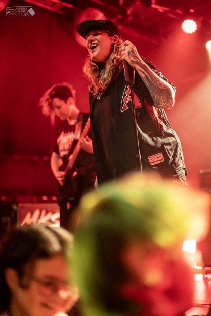 Interview mit Gero / Female Fronted is not a Genre Festival 2026 2 Eine in rötliches Licht getauchte Bühne zeigt zwei Musikerinnen. Eine spielt Girtarre, die andere hält ein Mikrophon und lacht.